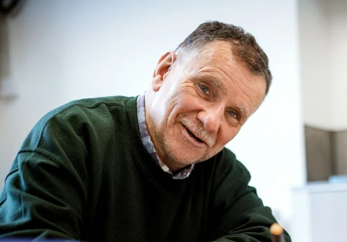 Man sitting at a table holding a pen looking happy